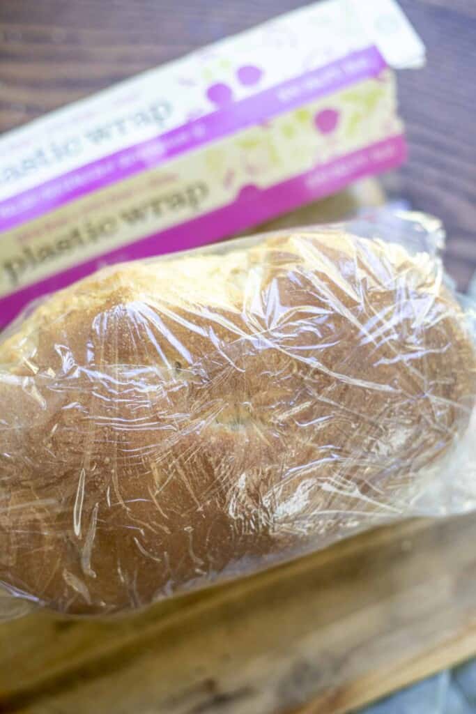 wrapping a loaf of bread in plastic wrap on a wood cutting board