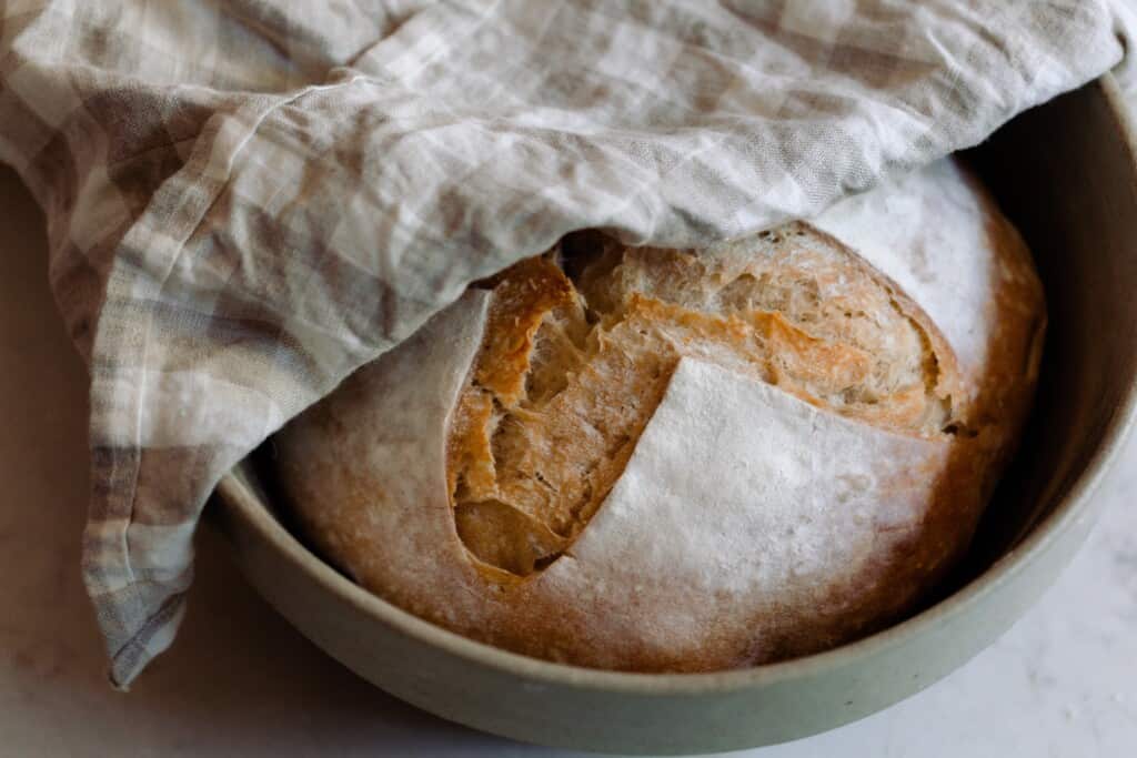 Sourdough boule in a green bowl with a plaid tea towel over half and folded over