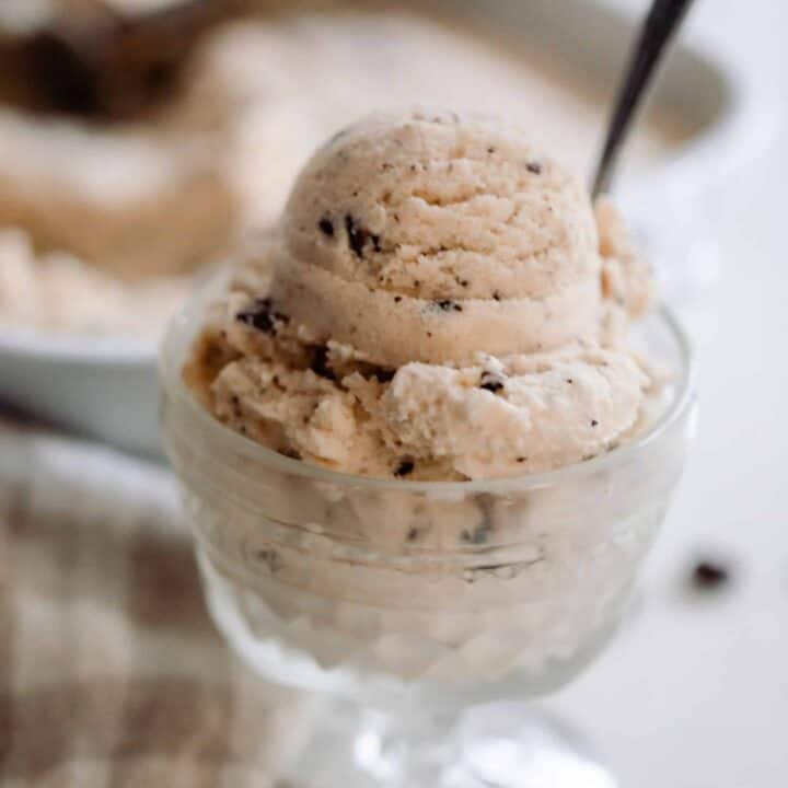 java chip ice cream scooped into a glass vintage ice cream dish with a spoon. The dish sits on a a white countertop op with a tan and white checked towel