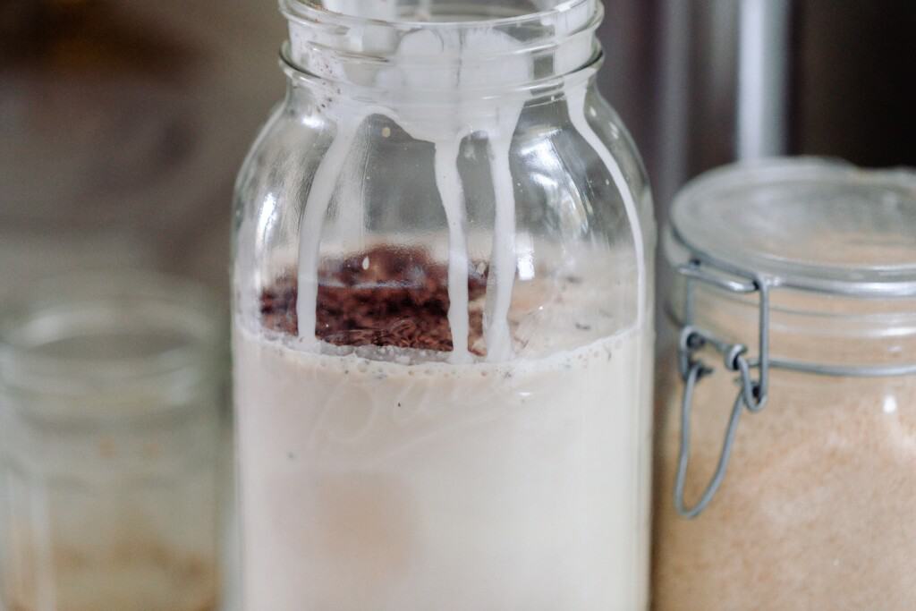 milk, cream, sugar, chocolate chips, and espresso in a half gallon mason jar with another jar or sugar to the left