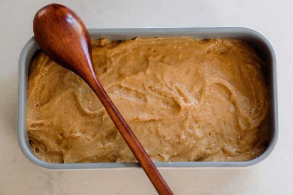pawpaw bread batter in a loaf pan with a wooden spoon resting on top