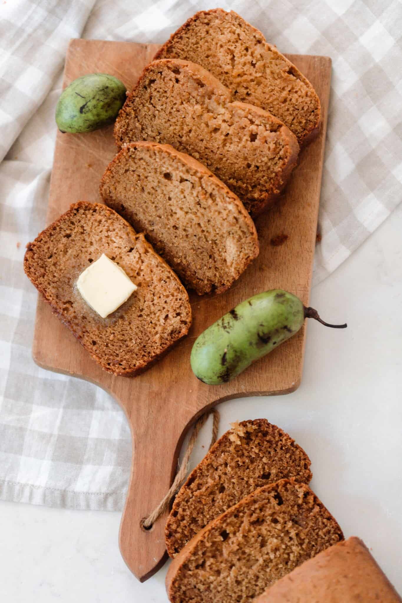 slices of pawpaw bread on a wooden cutting board on a white and tan checked towel