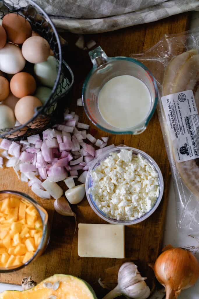 overhead photo of eggs, jars of milk, and cheese, onions, and halved pumpkin on a table