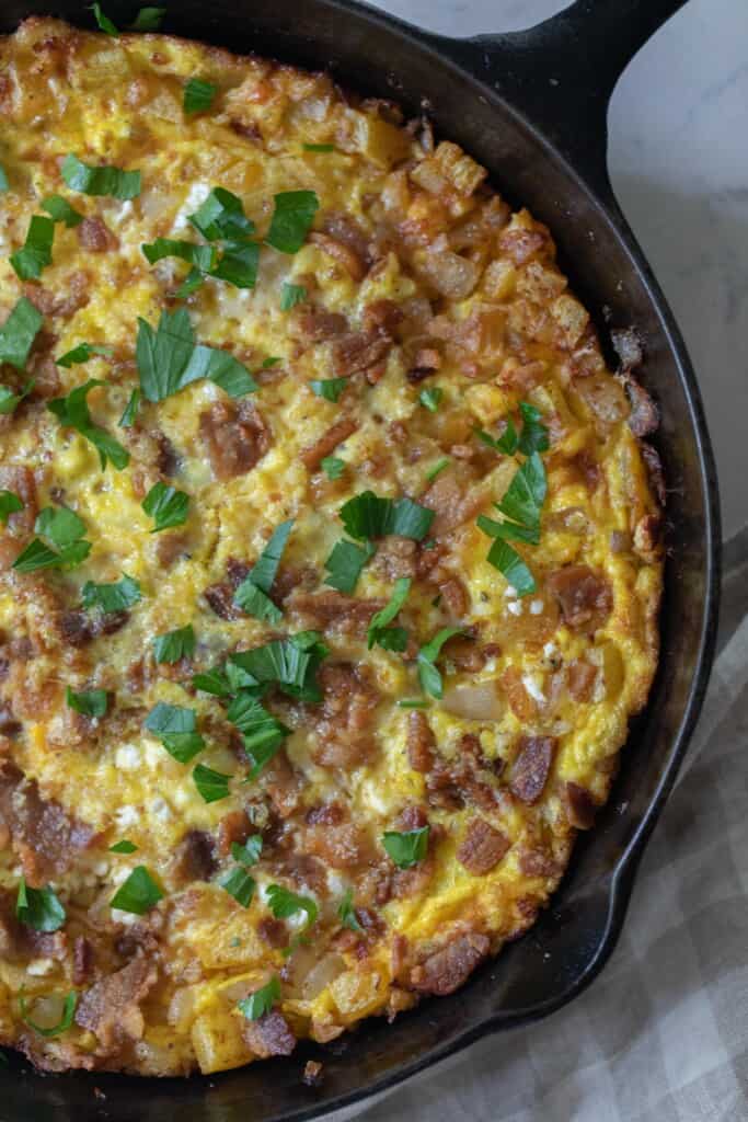 overhead photo of a pumpkin frittata topped with parsley in a cast iron skillet