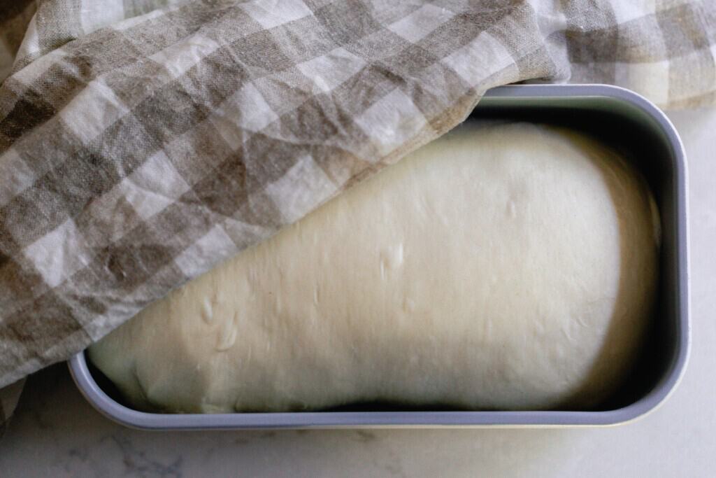 bread dough in a bread pan with a towel covering 1/4 of the loaf