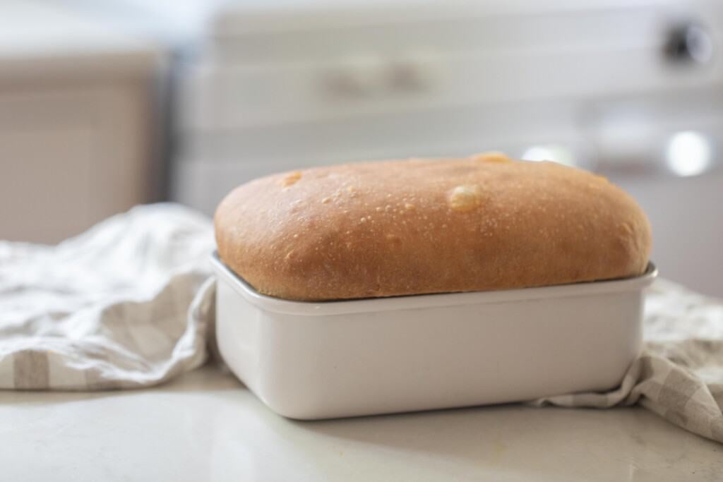 a loaf of sourdough discard sandwich bread in a white baking dish on a white countertop with a white vintage stove in the background