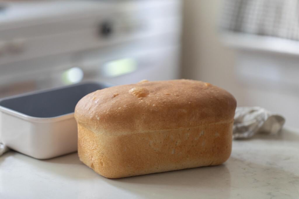 loaf of sourdough bread on a white countertop with a loaf pan in the background
