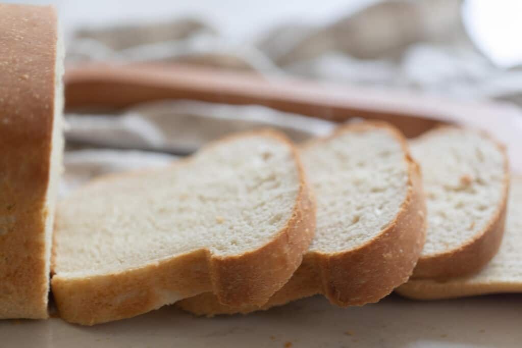 slices of sourdough discard sandwich bread on  a white quartz countertop with a towel and wooden bread knife in the background