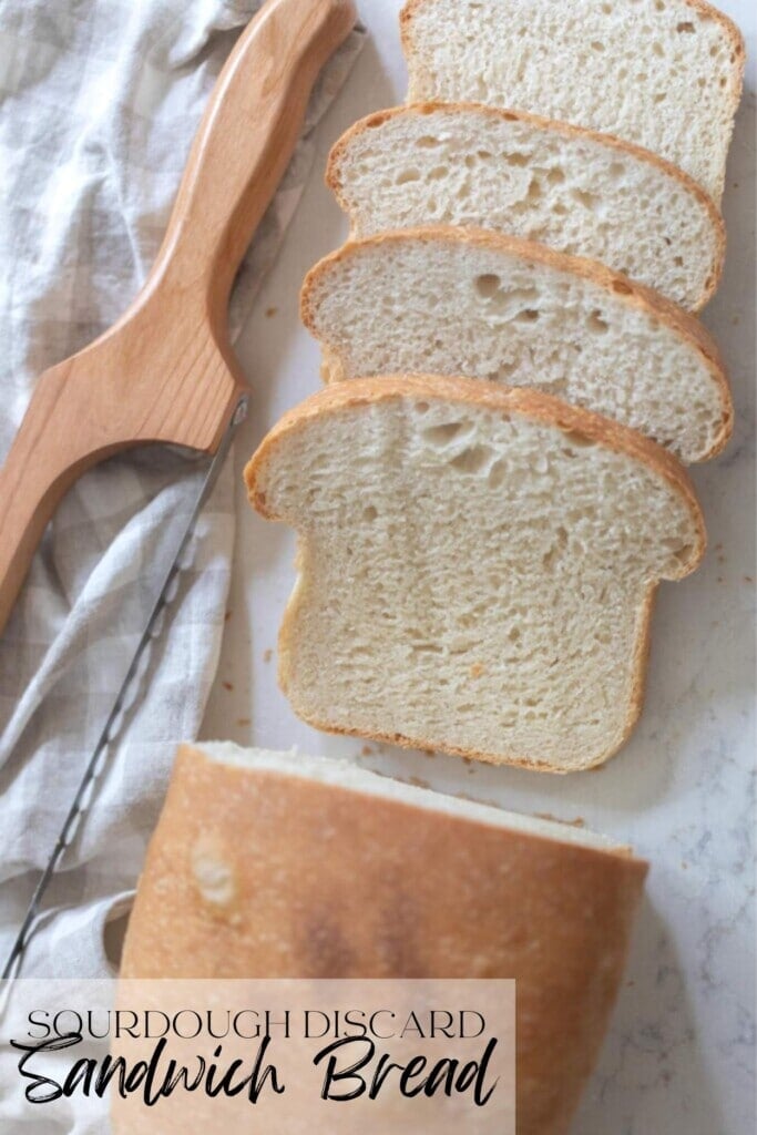 overhead photo of a loaf of sourdough sandwich bread with four slices off on white countertop with a towel and bread knife to the left