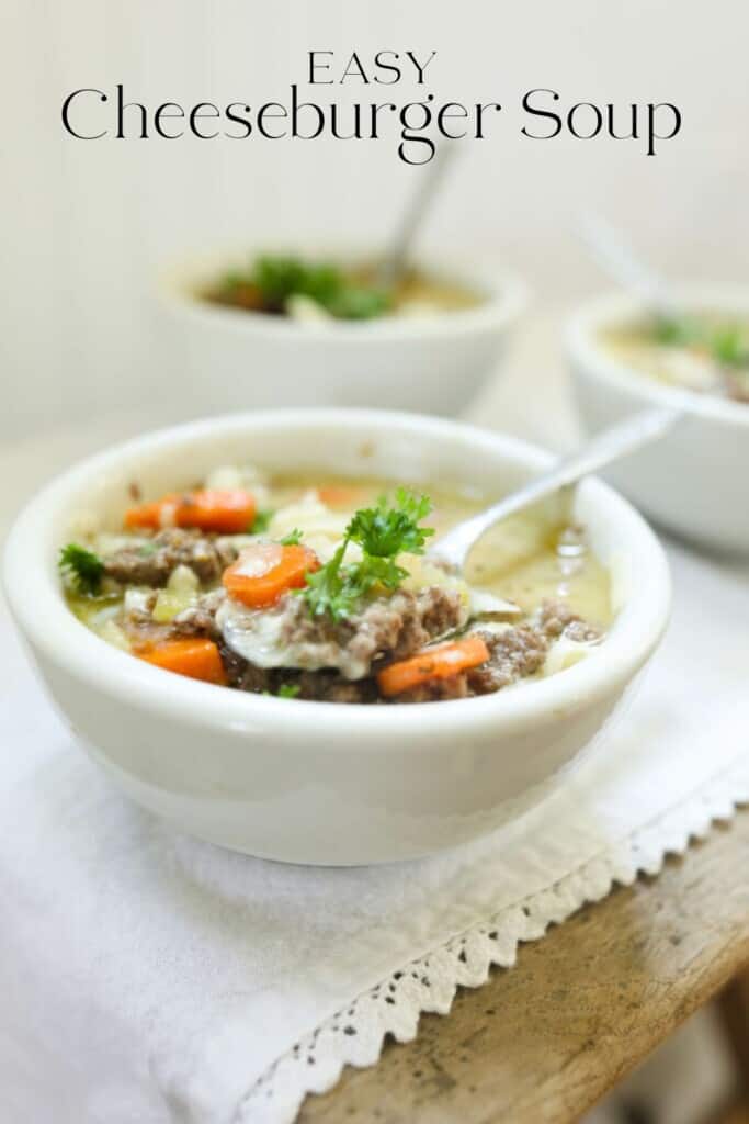 3 bowls of cheeseburger soup in white bowls with spoons on top of a wood table with white table runner.