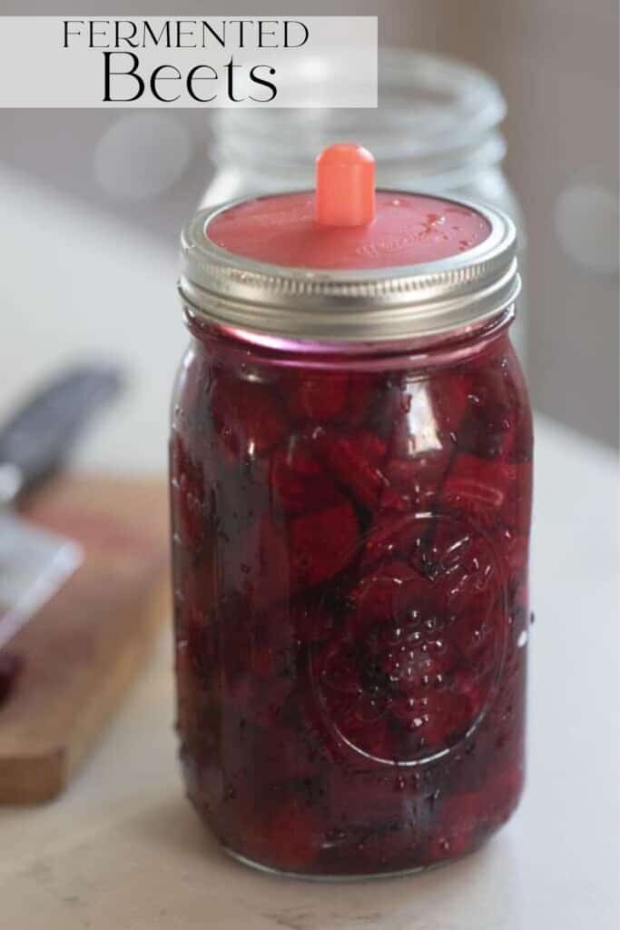 fermented beets in a glass mason jars with a silicon fermenting lid on a white countertop with a cutting board to the left