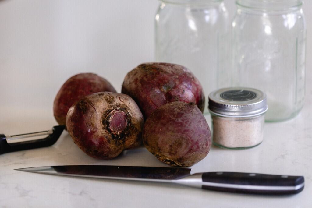 beets, salt, jars and a knife on a white countertop