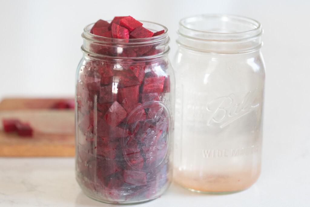 chopped beets added to a quart jar. Another quart jar with salt water is to the right