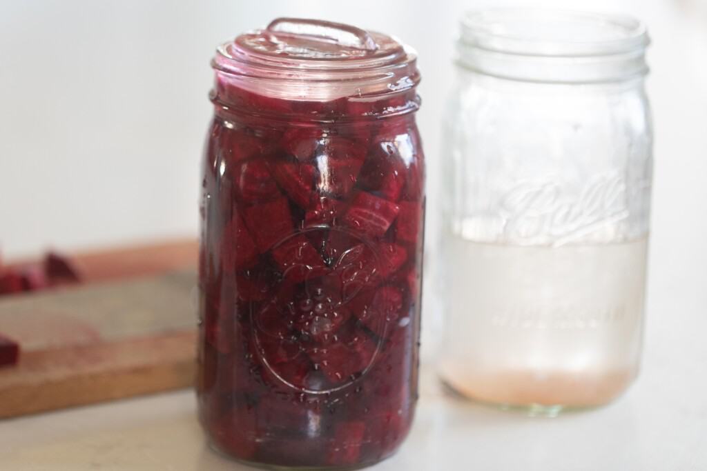 brine and beets in a quart jar with a glass weight on top with another quart jar to the right