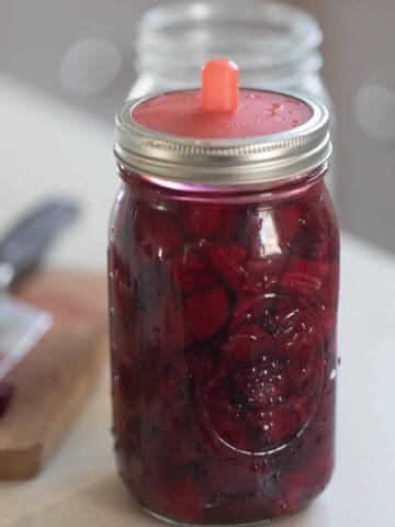 fermented beets in a glass mason jars with a silicon fermenting lid on a white countertop with a cutting board to the left