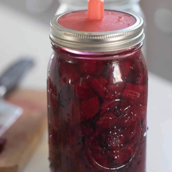 fermented beets in a glass mason jars with a silicon fermenting lid on a white countertop with a cutting board to the left