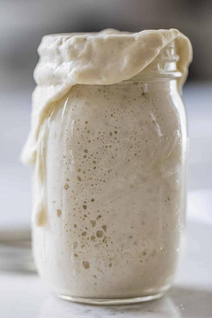 sourdough starter overflowing out of a mason jar on a white countertop