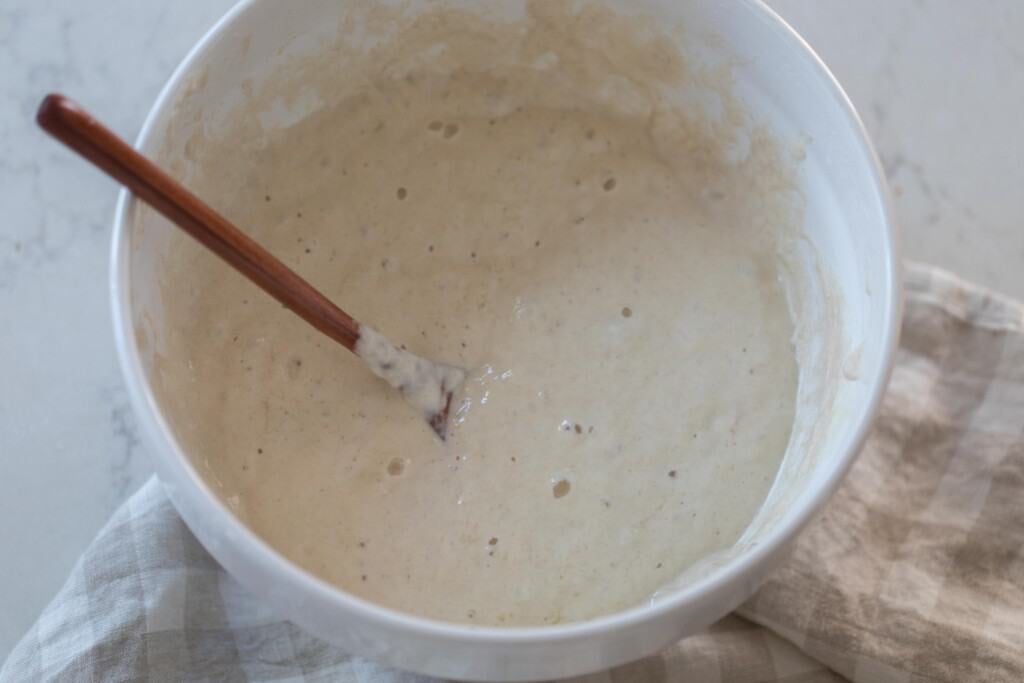 crumpet batter in a stoneware bowl with a wooden spoon