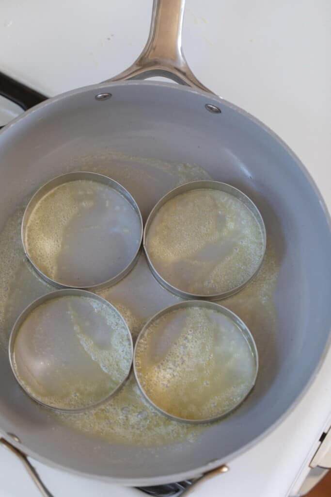 heating English muffin rings in a skillet with butter