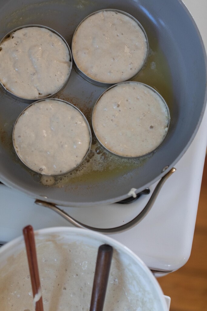 crumpets cooking in English muffin rings in a caraway pan