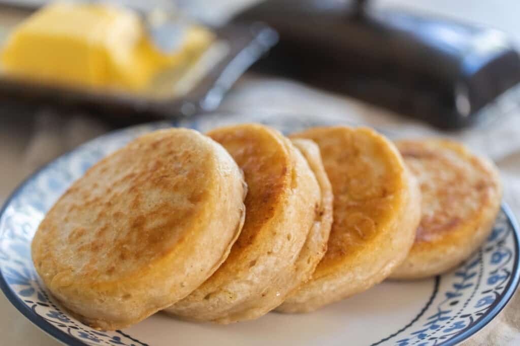 four sourdough crumpets lined up on a blue and white plate with butter in the background
