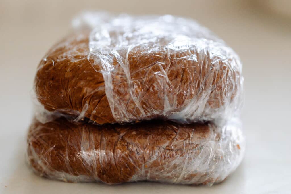 two discs of gingerbread dough wrapped in plastic on a white countertop 