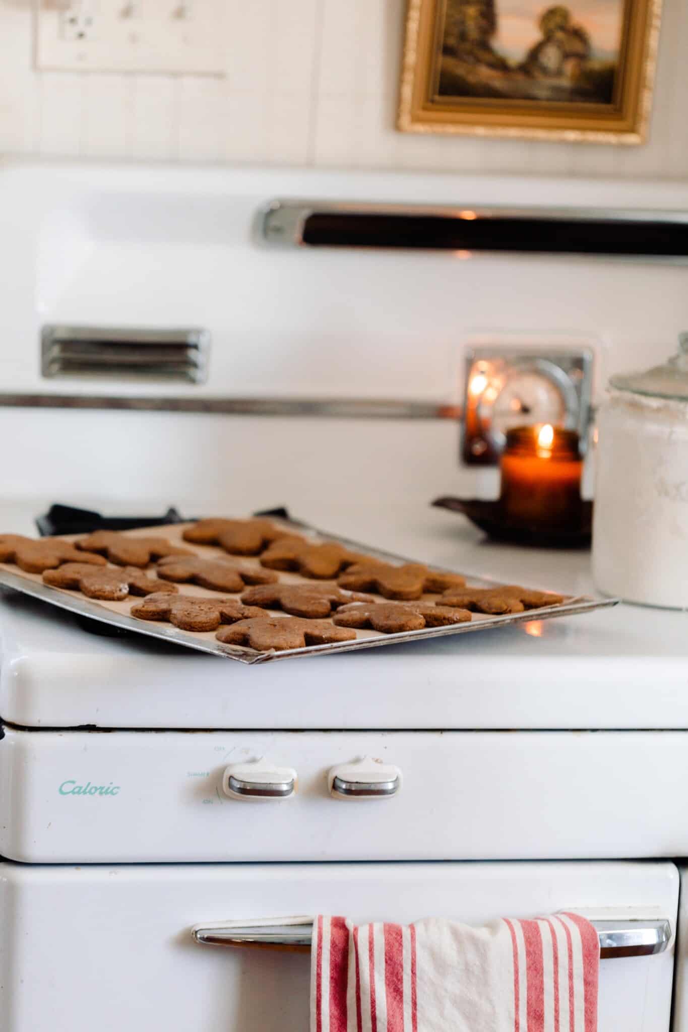 sourdough gingerbread cookies on a baking sheet on a vintage stove with a candle burning