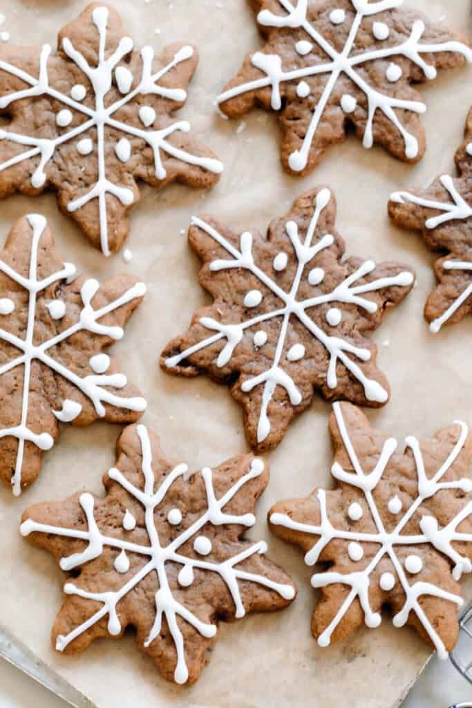 overhead photo of decorated sourdough gingerbread cookies in the shape of a snowflake  on parchment paper
