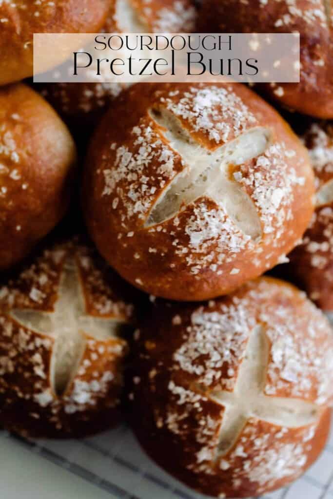 sourdough pretzel buns topped with course salt stacked on a white countertop