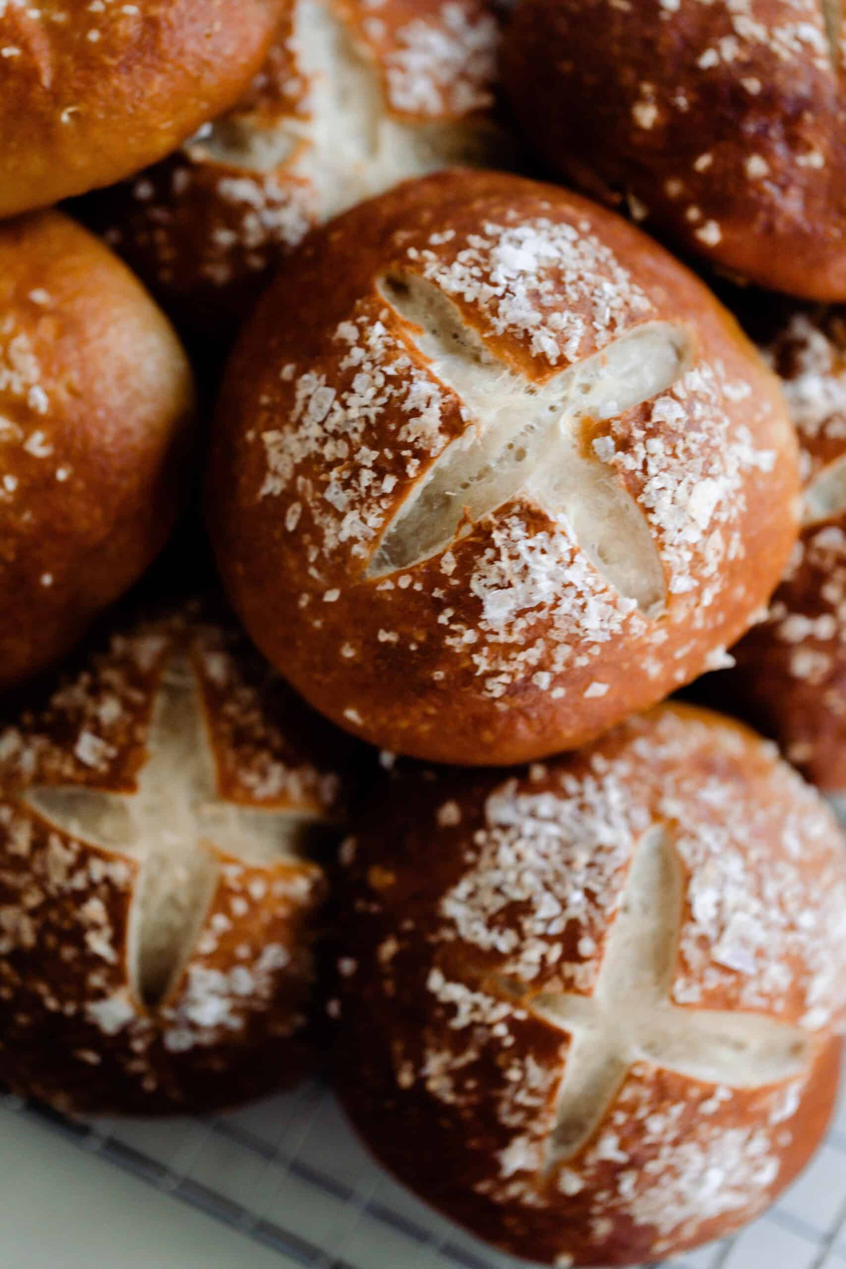 sourdough pretzel buns topped with course salt stacked on a white countertop