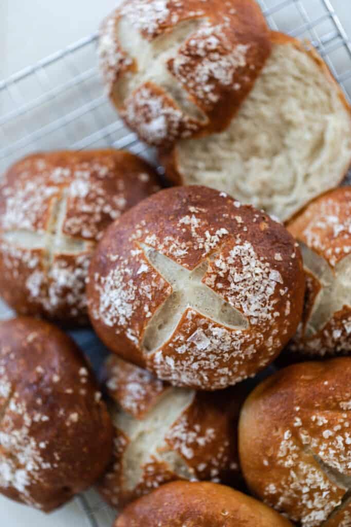 overhead photo of sourdough pretzel buns on a white towel. One bun is cut in half