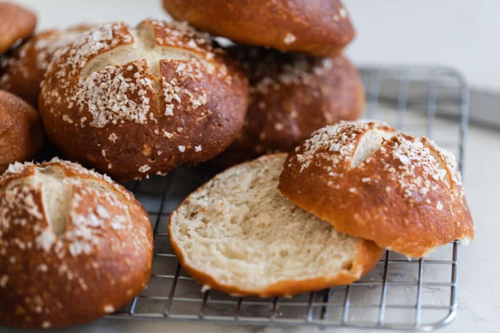 sourdough pretzel buns on a wire rack. One bun is slice in half