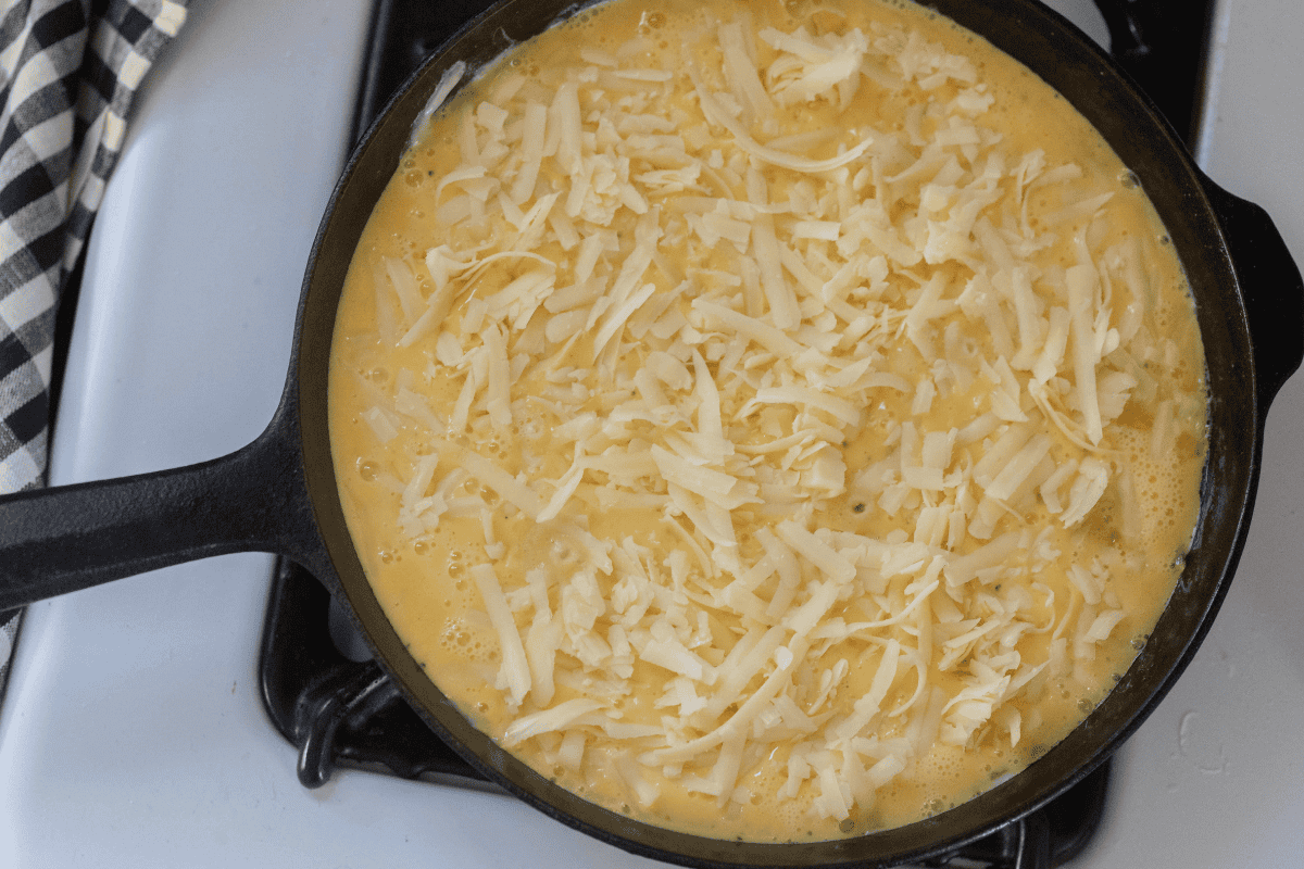 Cast iron skillet on a white stove filled with the frittata mixture and cheese.
