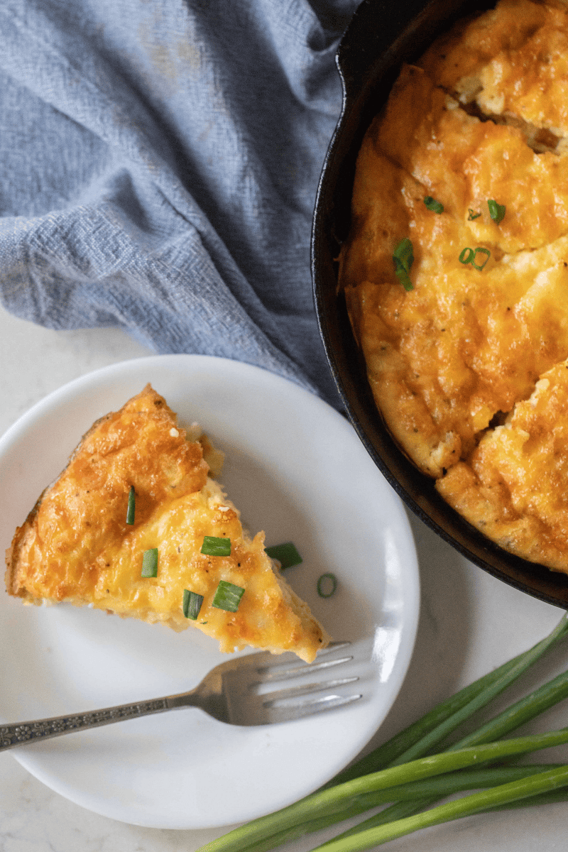 A cast iron skillet with a baked ham and cheese frittata and green onions on top.