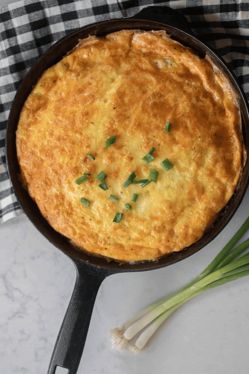 A cast iron skillet with a baked ham and cheese frittata and green onions on top.