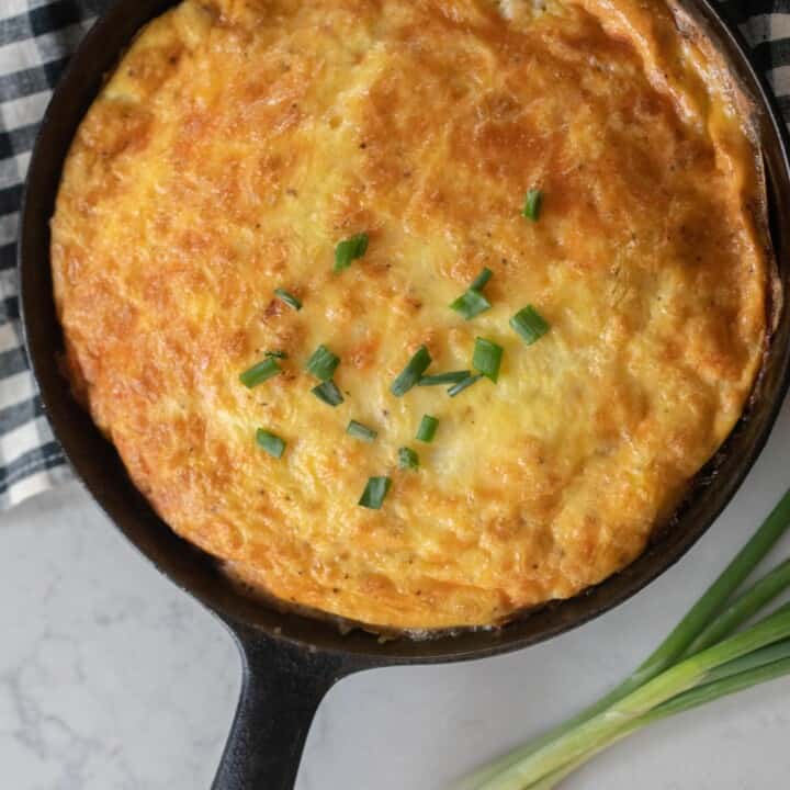 Ham and cheese frittata in a cast iron skillet on a blue and white checkered tea towel