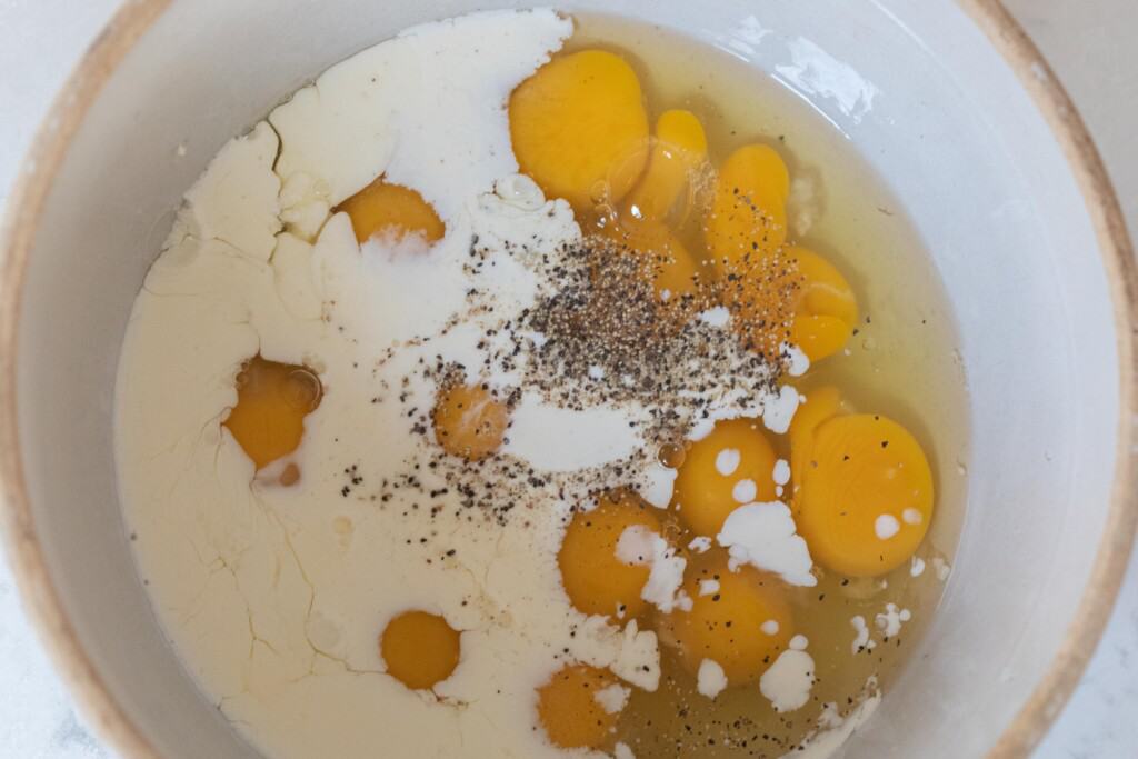 Eggs, milk, salt and pepper in a large white bowl ready to be whisked together