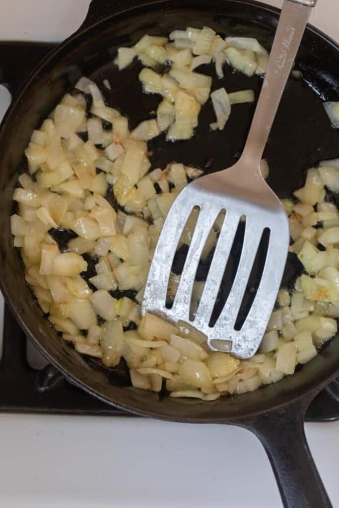 Onions cooking in a cast iron skillet with a metal spatula 