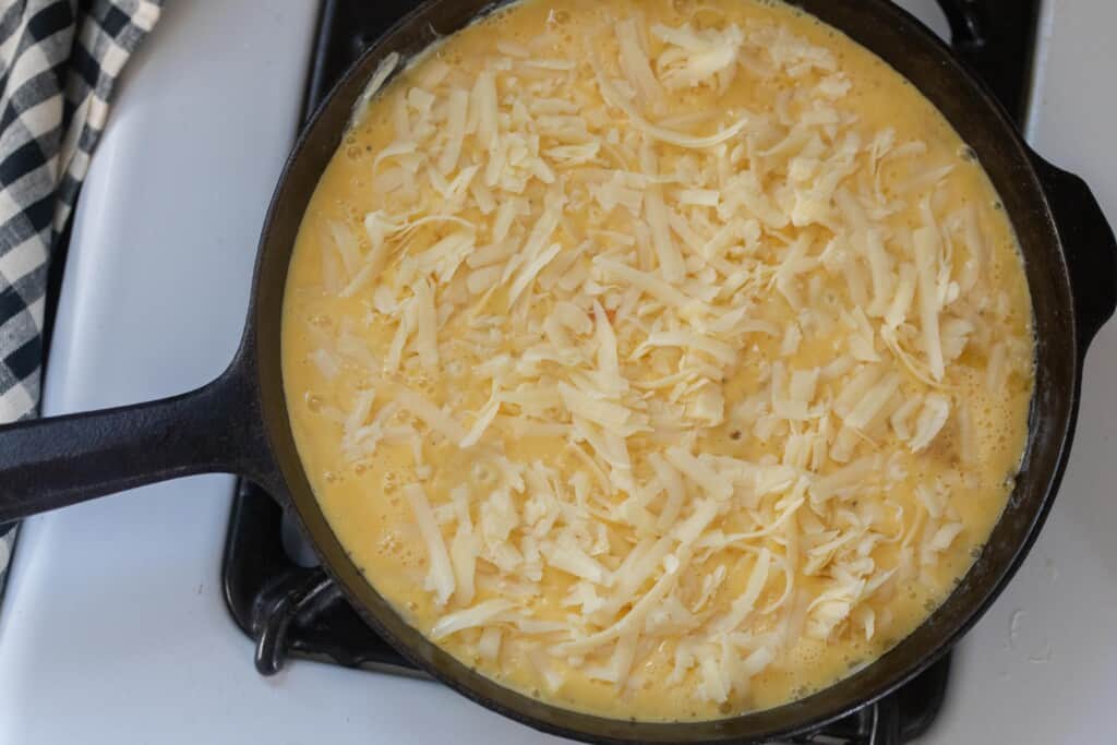 Cast iron skillet on a white stove filled with the frittata mixture and cheese