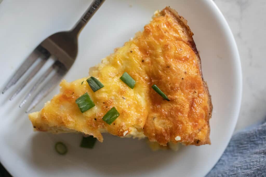 Slice of ham and cheese frittata on a white plate with a silver fork