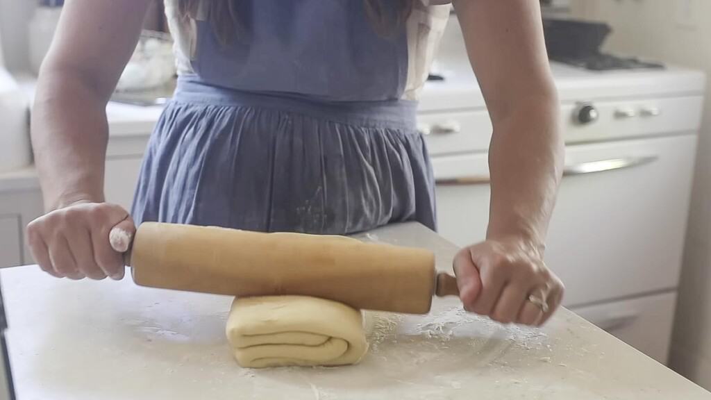 rolling out the folded pastry dough on a floured white counter top