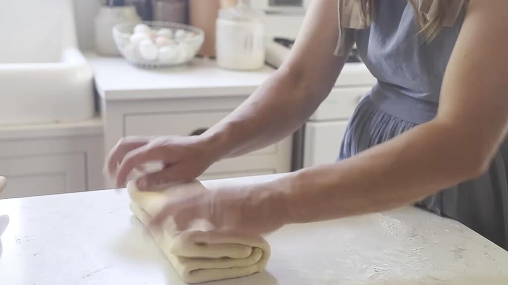 folding pastry dough up into four layers  on a white countertop