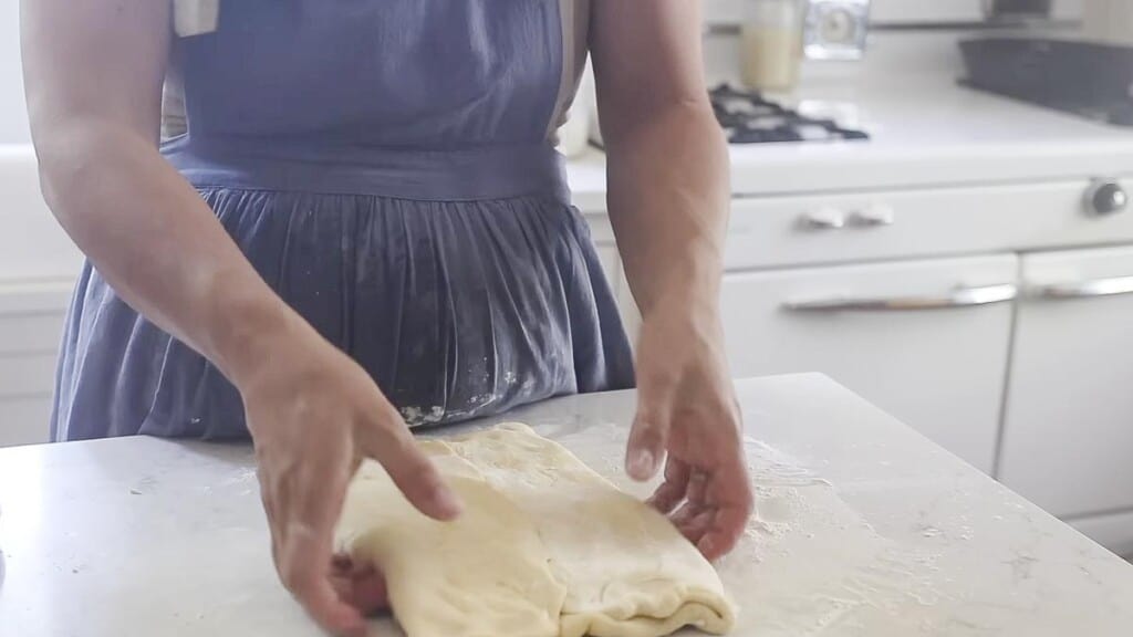 folding dough over the rectangle of butter on a white countertop