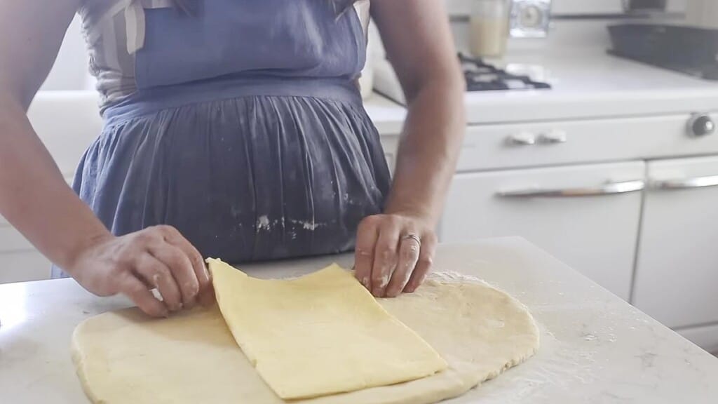 placing rolled out butter in the middle of dough on a white countertop