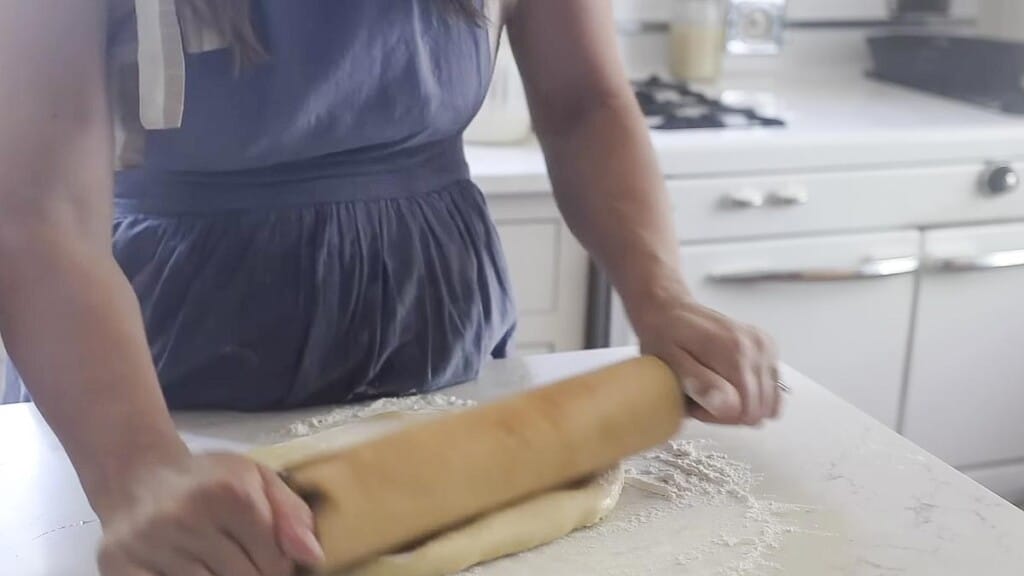 rolling out dough on a white floured countertop 