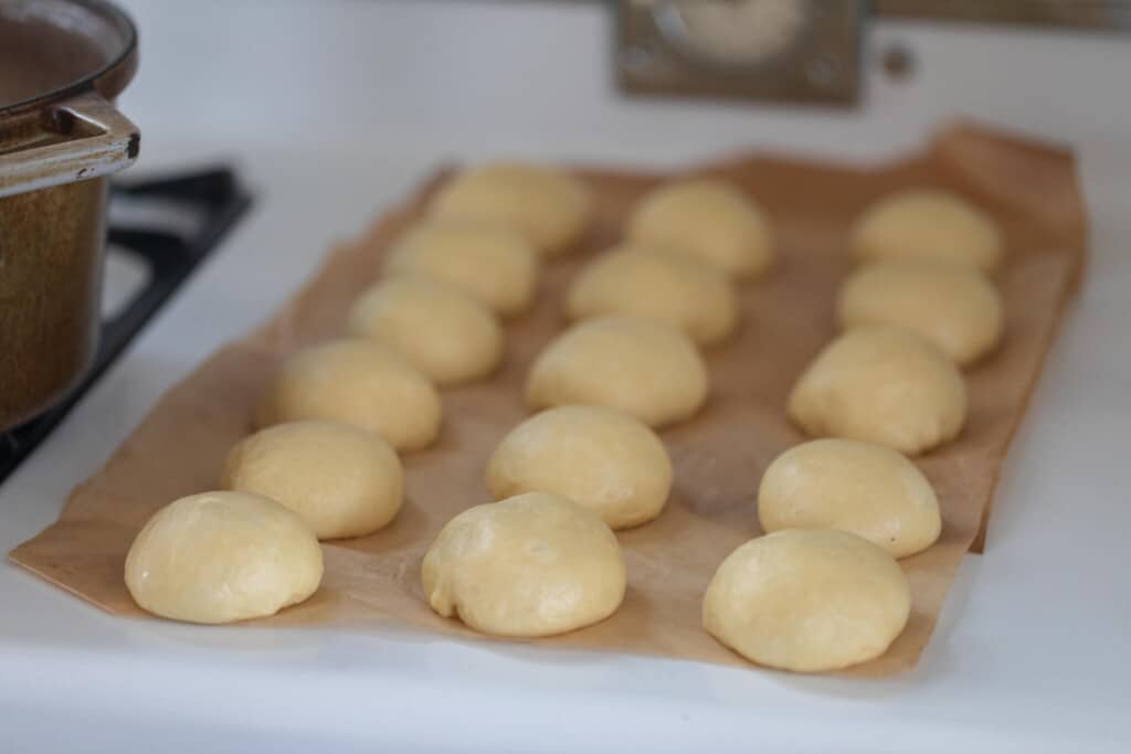 brioche donut dough balls on parchment paper on a white countertop