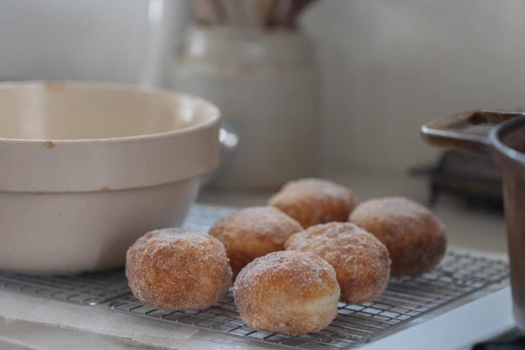 Brioche donuts tossed in sugar on a wire rack with a ceramic bowl next to them