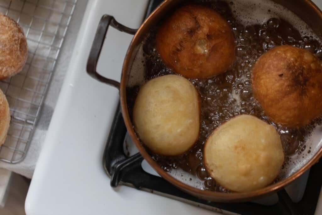 Donuts frying in a pot with a wire rack next to it
