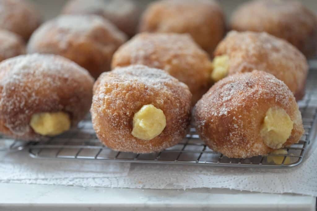 Brioche donuts with custard filling sitting on a wire rack to cool on a white counter top