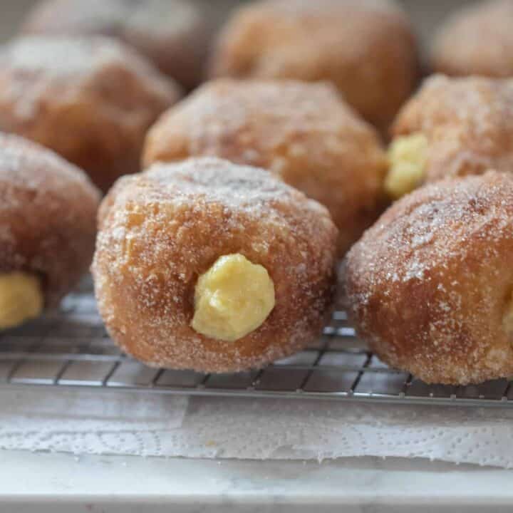 Brioche donuts with custard filling sitting on a wire rack to cool on a white counter top
